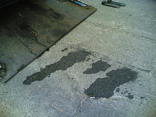 The image shows several oil or fluid stains on a concrete floor.