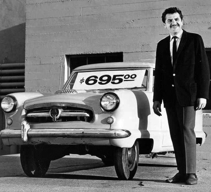 Man standing beside an old car with a $695 price sign in the windshield