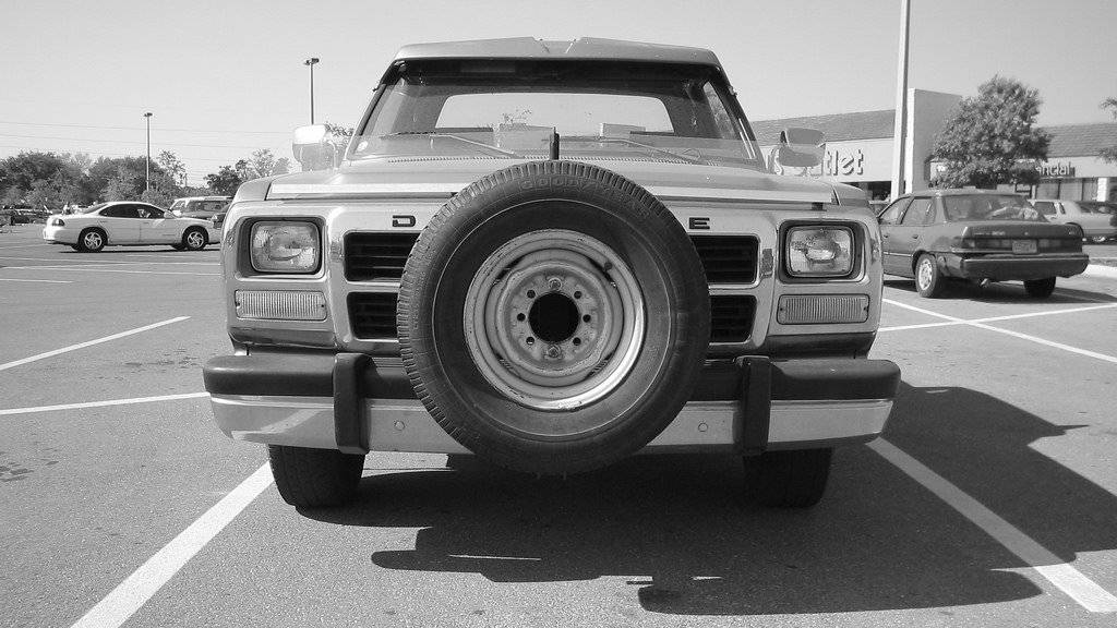 Front view of a vehicle with a spare tire mounted on its grille in a parking lot