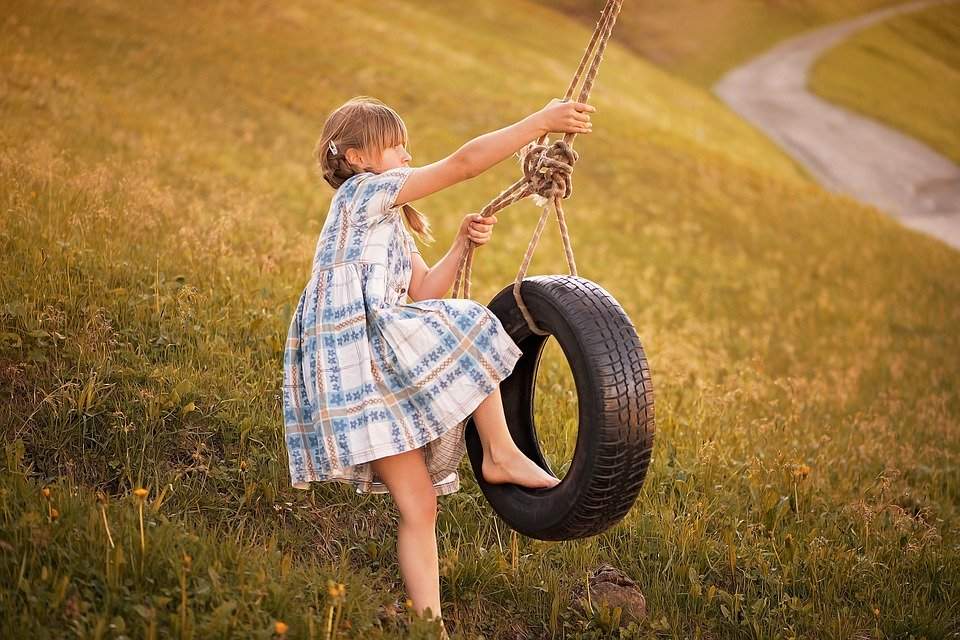 A young girl playing on a tire swing outdoors.