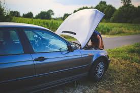 Person inspecting the engine of a car with the hood open, parked by the roadside