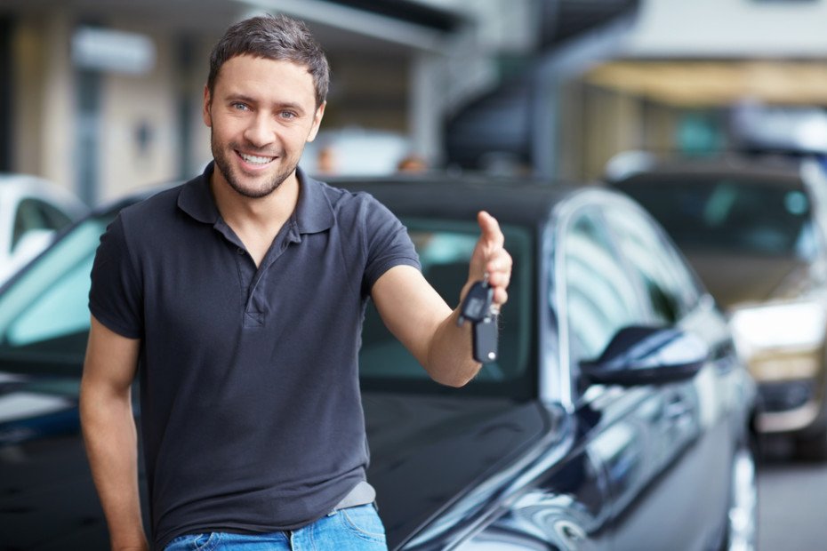 Smiling man holding car keys while standing next to a car.